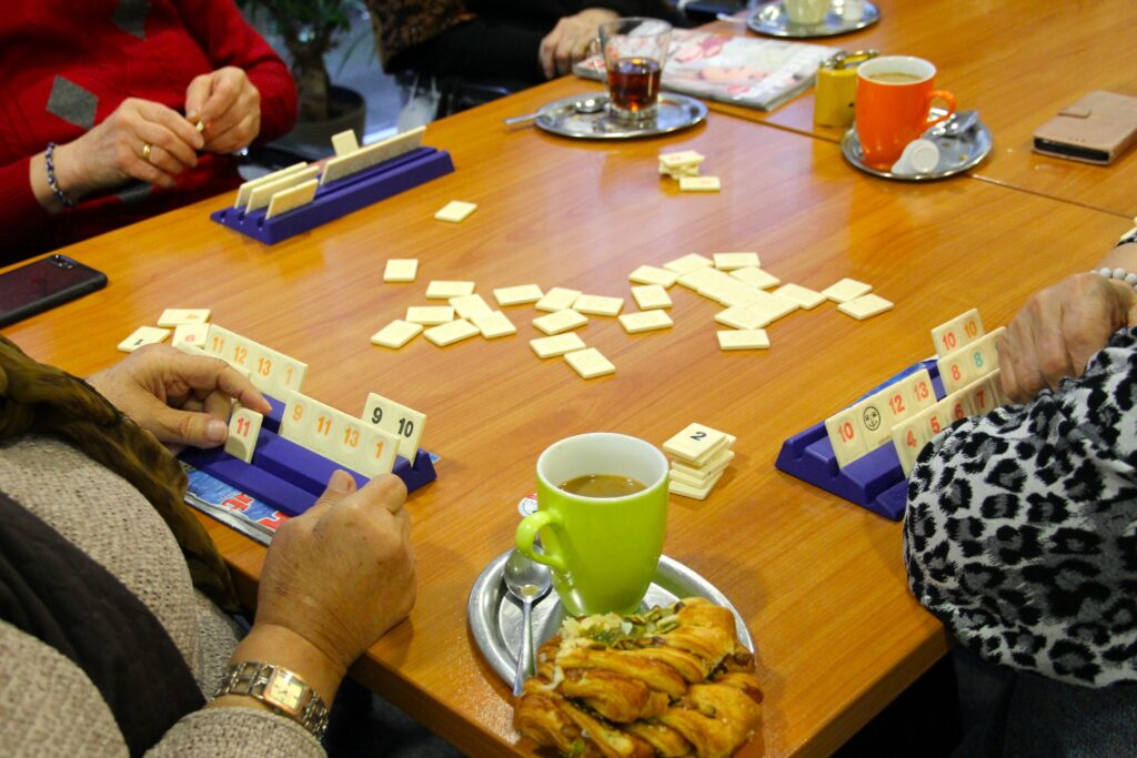 Besucher des Nachbarschaftsheims St. Pauli beim gemeinsamen Spielen. Zu erkennen sind nur Hände, das Spiel Rummikub, Kaffee & Tee