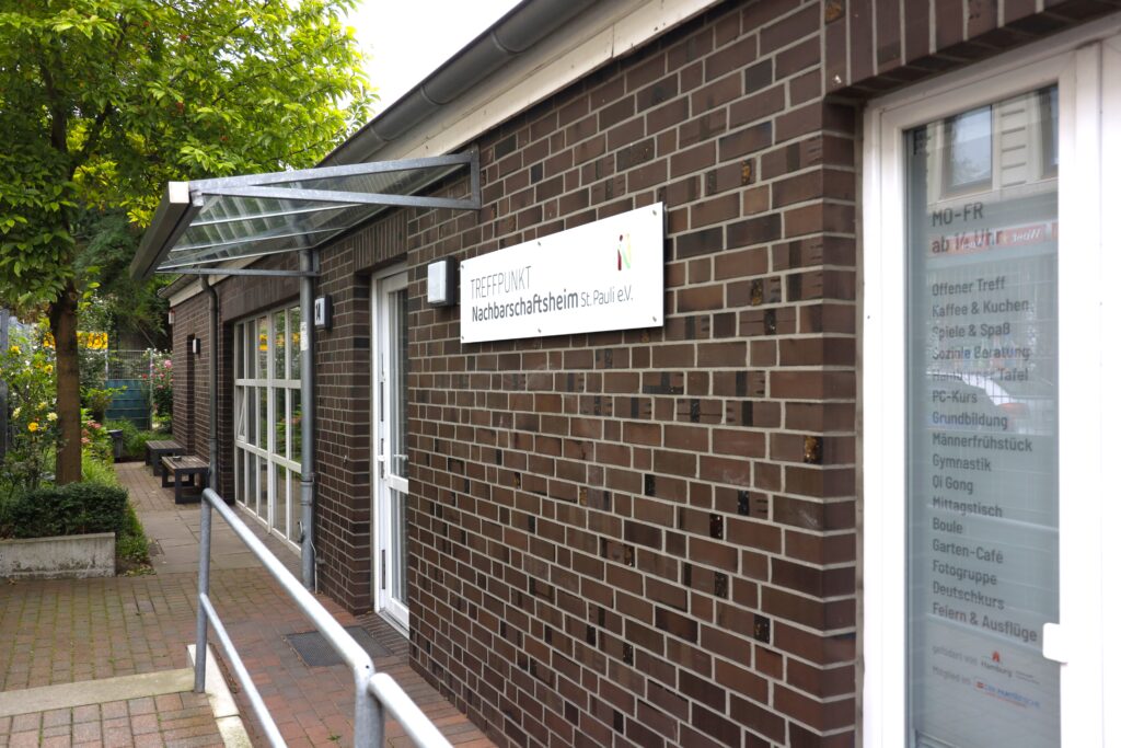 Außenaufnahme des Nachbarschaftsheims St. Pauli. Zu erkennen das Schild "Treffpunkt Nachbarschaftsheim St. Pauli e.V." und eine Angebotstafel "Mo-Fr ab 14 Uhr"