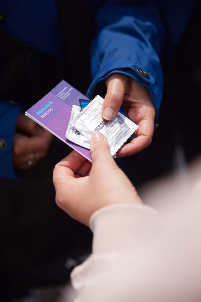 Zwe Hände, überreicht werden ein Flyer des Sperrgebiet Hamburg und zwei Kondome