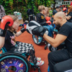 Auf einem Sportplatz sind Kinder im Rollstuhl, die Boxhandschuhe tragen. Im Vordergrund: Kareem Ahmed mit Pratzen