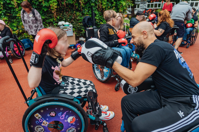 Auf einem Sportplatz sind Kinder im Rollstuhl, die Boxhandschuhe tragen. Im Vordergrund: Kareem Ahmed mit Pratzen