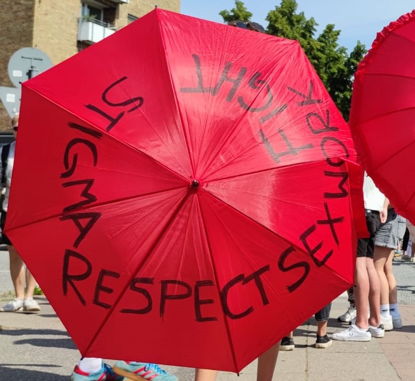 Menschen tragen rote Regenschirme, auf denen "Respect Sexword, Fight Stigma" steht