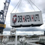 Ein Container am Kran, der Container per Bildbearbeitung beschriftet mit "Der Hafen hilft"